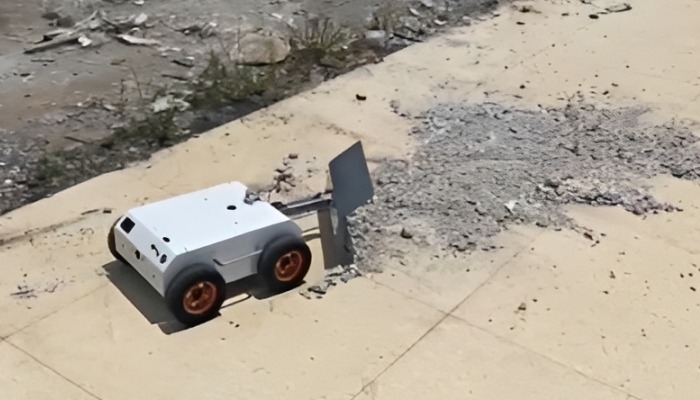 Robot with plow blade clearing gravel on concrete