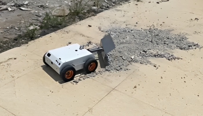 Robot pushing pile of gravel across pavement
